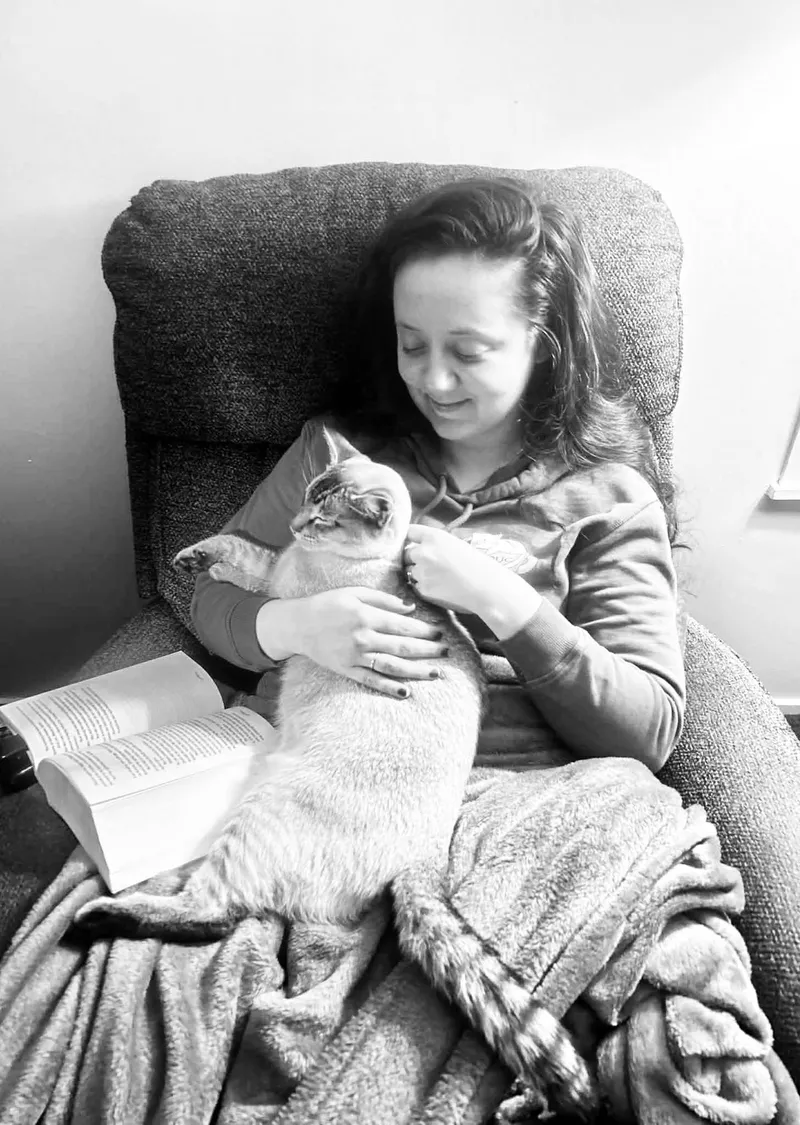 Katrin Chisholm reading in an armchair with her cat